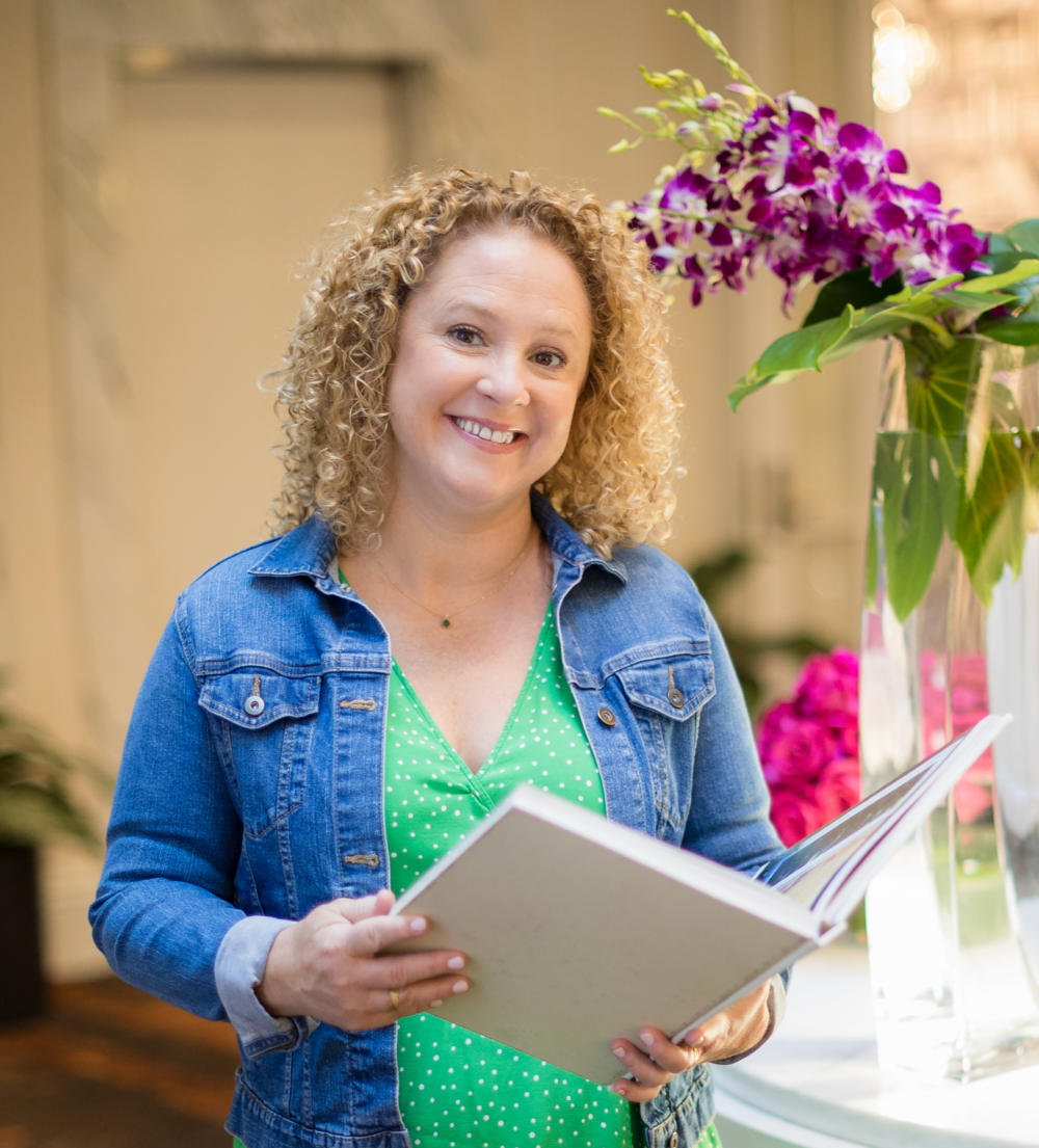 Andrea Guevara, the author brand strategist and expert, standing near flowers with a book in her hands